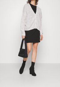 Světle šedý pletený kardigan s výstřihem do V, černé přiléhavé šaty, černé kotníkové boty na podpatku a malá černá kabelka přes rameno.