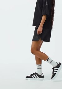 Čierny športový outfit pozostávajúci z voľného trička a šortiek. Čierno-biele tenisky so tromi pruhmi a biele ponožky s logom.