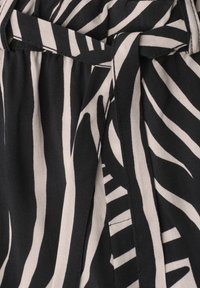 Tissu noir et blanc avec des rayures audacieuses semblables à celles d’un zèbre, avec un détail de ceinture en tissu nouée au centre.