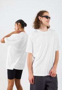 Bílé oversized trička vyrobené z bavlny, s krátkými rukávy a kulatým výstřihem, vystavené na dvou modelech z předního a zadního úhlu.