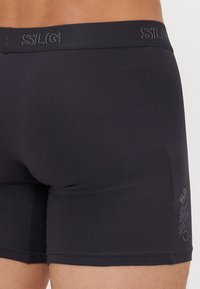 Zwarte boxershorts van gladde stof, met een brede tailleband met reliëfbranding en gestikte naden. Minimalistisch ontwerp.