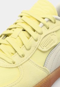Gule semskede sneakers med teksturerte lisser, hvite detaljer og en beige såle. Har preget logo på sidepanelet og glatt tåhette.