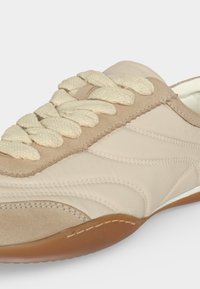 Baskets beige et marron clair avec des lacets crème épais, des détails en suède texturé, des motifs de couture et une semelle en caoutchouc marron.