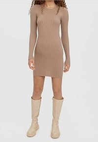 Ribbad stickad klänning i mjuk beige med långa ärmar, rund halsringning och figurnära siluett, kombinerad med knähöga beige stövlar.