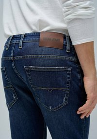 Tamno plavi traperici s kontrastnim šavovima i smešnim kožnim etiketom "Salsa Jeans" na pojasu. Sadrže dva zadnja džepa.