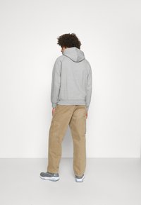 Grauer Hoodie mit Kapuze und geripptem Saum, kombiniert mit beigen Cargo-Hosen mit Taschen, vor einem schlichten weißen Hintergrund.