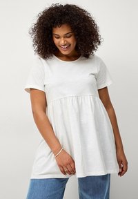 Hellbeige T-Shirt aus weichem Stoff, mit rundem Halsausschnitt und kurzen Ärmeln, und einer gerafften Taille für eine lockere Passform.