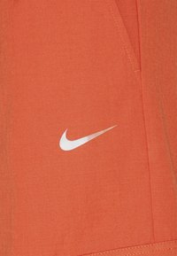 Nike-kläder i en ljus orange tyg har en texturerad finish och en liten, vit Nike-swoosh-logotyp på sidan.