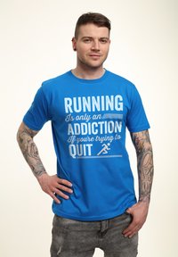 Camiseta de algodón azul con texto impreso en blanco: “CORRER es solo una ADICCIÓN si estás intentando DEJARLO” y un ícono de carrera.
