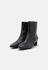 Botine negre din piele cu o textură netedă, vârf ascuțit și un toc mic de tip bloc. Design simplu, fără hardware sau accente vizibile.