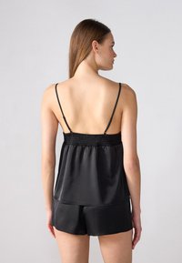 Fekete selyem camisole vékony pántokkal és ráncolt felsőrésszel, hozzá illő rövidnadrággal párosítva. Sima textúra, laza fazon, minimalista dizájn.