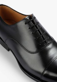Zapato de vestir de cuero negro con cordones que presenta una textura suave, punta redondeada y detalles sutiles de costura en la parte superior. Diseño sencillo y clásico.
