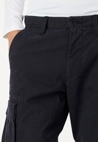 Pantaloni cargo de culoare bleumarin închis, dintr-un material durabil, prevăzuți cu închidere cu buton, buzunare laterale și cusături călcate pentru o structură îmbunătățită.