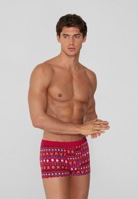 Baúl rojo con patrón de diseños geométricos y florales, hecho de tela suave. Presenta un corte ajustado y una pretina a contraste para mayor detalle.