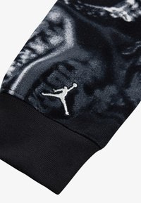 Čierna bavlnená mikina s dlhým rukávom, ktorá má textúrovaný vzor, manžetu s rybím vzorom a na boku vyšívané logo Jumpman v bielej farbe.