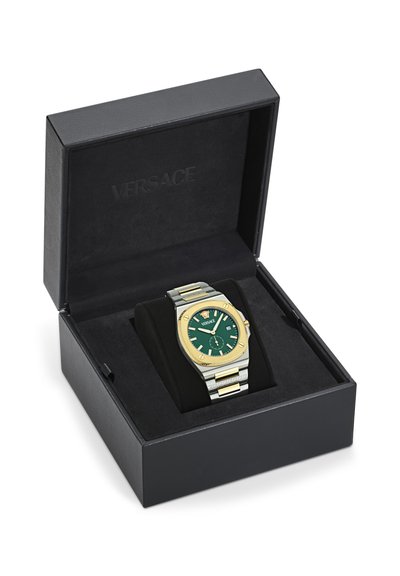 Orologio oro e argento con quadrante verde in una scatola nera Versace aperta. L'orologio presenta un quadrante testurizzato e una funzione data.