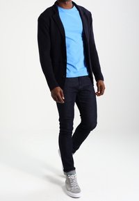 Námořnické texturované sako přes světle modré tričko, doplněné tmavými džínami a šedými teniskami se šněrováním a kulatou špičkou.