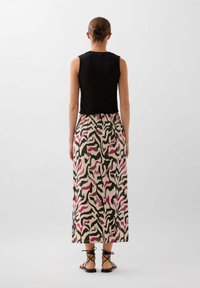 Schwarzes ärmelloses Top, kombiniert mit einem gemusterten Maxikleid in Creme, Pink und Schwarz; verfügt über eine taillierte Taille und flache Sandalen.