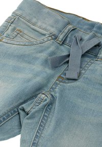 Světlé modré džíny z denimu s jemnou texturou, s páskem na zavázání, předními kapsami a kontrastním žlutým šitím.