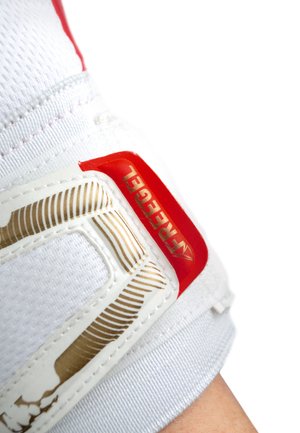 Guanto sportivo bianco con grip testurizzato, dettagli rossi e dorati, e una cinghia di chiusura sicura. Il materiale sembra flessibile e traspirante.