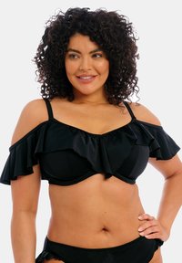 Top bikini nero con maniche a sbuffo off-the-shoulder, tessuto liscio e design strutturato. Caratterizzato da una scollatura a cuore e spalline regolabili.