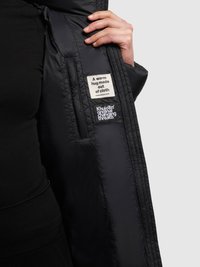 Sort puffervest med quiltet design, med et mærke der lyder "En varm kram lavet af stof" og logopatche indvendigt.