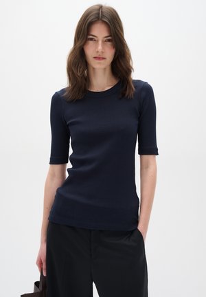 Top corto a maniche corte in maglia a coste di colore blu navy con scollo rotondo e silhouette aderente, abbinato a pantaloni neri. Tessuto dal tratto liscio.