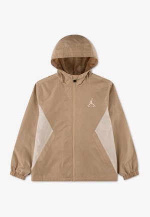 Coupe-vent beige à capuche avec fermeture éclair frontale, panneaux latéraux blancs, poignets élastiques et petit logo Jordan blanc sur la poitrine gauche.