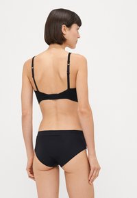Crni bikini gornji i donji dio, bez šavova, podesive naramenice, glatka tekstura. Pogled straga koji prikazuje minimalistički stil i sigurnu prilagodbu.