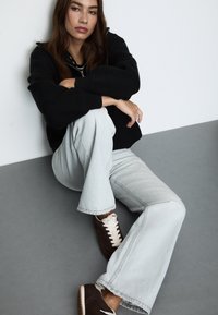 Črna kapuca, svetlo sivi široki traperji in temnosnedeži superge s kremnimi vezalkami. Gladek material in sproščen kroj.