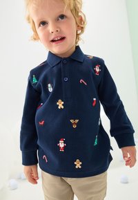 Donkerblauw poloshirt met lange mouwen, voorzien van kleurrijke borduursels met feestthema, waaronder rendieren, de kerstman en bomen. Lichtgewicht katoenmengsel.