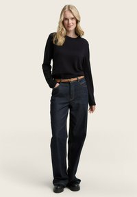 Jean en denim bleu foncé avec une coupe décontractée, taille haute et couture jaune contrastante, assorti à un haut noir à manches longues et une ceinture marron.
