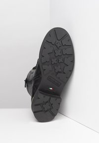 Black leather boot with a textured black rubber sole featuring a tread pattern, side zipper, and branding detail near the bottom.