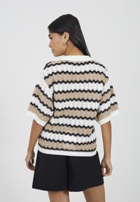 Sweter dzianinowy z otwartym wzorem w faliste paski w kolorach beżowym, białym i czarnym. Krótkie rękawy oraz rypsowe wykończenie.