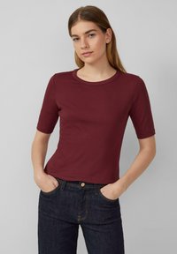 Bordeaux kortemouwen t-shirt met een ronde halslijn, gemaakt van een soepele, rekbare stof, gecombineerd met donkerblauwe spijkerbroek.