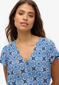 Vestido con estampado floral en tonos de azul y blanco, con escote en V y mangas cortas con puños enrollados. Detalle de botones en la parte delantera.