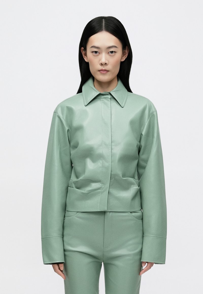 Casaco de pele sintética verde menta com gola, mangas compridas e bolsos frontais, combinado com calças ajustadas da mesma cor.