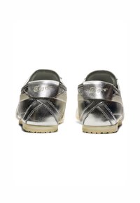 Baskets métalliques argentées avec un design à coupe basse. Elles présentent une texture lisse, des coutures contrastantes et une semelle en caoutchouc beige.