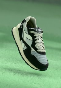 Crne i sive sportske cipele s gornjim dijelom od mrežaste tkanine i antilopa, s bijelim vezicama, uzorkovanom jezičkom i debelim gumenim potplatom.