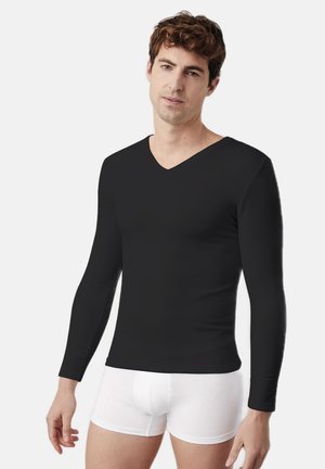Camisa negra de manga larga con escote en V, hecha de un tejido suave y con un diseño entallado. Llevada con calzoncillos blancos. Estilo minimalista, sin patrones.
