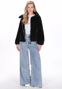 Czarna kurtka polarowa z zamkiem z przodu, dużymi rękawami i kapturem; zestawiona z niebieskimi dżinsami o szerokich nogawkach i koszulą w paski.