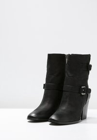 Botas negras de tobillo hechas de cuero texturizado, con cremallera lateral, una correa con detalle de hebilla y un tacón medio.
