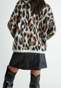 Pull en tricot avec imprimé léopard dans des nuances de noir, marron et crème. Associé à une mini-jupe en simili cuir noire et des bottes brillantes jusqu'aux genoux.