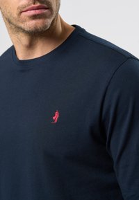 Camicia a maniche lunghe blu navy realizzata in cotone morbido, con scollatura rotonda e un piccolo logo rosso ricamato sul petto.