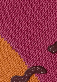 Zbliżenie na dzianinę z ukośnymi pomarańczowymi i fioletowymi sekcjami oraz ciemnobrązowymi falistymi liniami na fioletowej części.