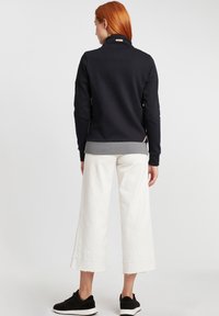 Felpa blu navy con colletto alto, fondo a costine grigio e spacchi laterali. Abbinata a pantaloni bianchi larghi e sneakers nere.