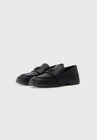 Pantofi loafers negri din piele netedă, cu o curea lată pe partea superioară, vârf rotund și talpă plată din cauciuc. Detaliu subtil cu logo inclus.