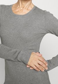 Szary, prążkowany top z długim rękawem i okrągłym dekoltem. Materiał wydaje się miękki, z dopasowanym krojem, ukazującym teksturowaną powierzchnię.