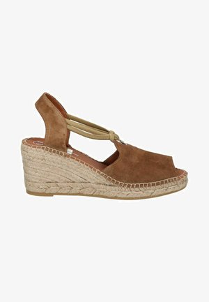 Sandalias con cuña de ante marrón, con una correa de tobillo elástica, punta abierta y suela de yute trenzado, presentando un diseño redondeado y un acabado texturizado.