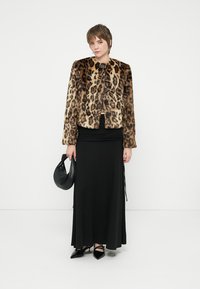 Leopárdmintás műszőrme kabát fekete gombokkal, fekete, testhezálló ruhával és fekete kézitáskával párosítva, egyszínű fehér háttér előtt áll.